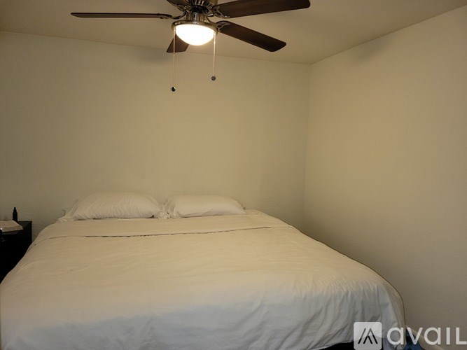 A bed with white sheets and pillows in a room with a ceiling fan.
