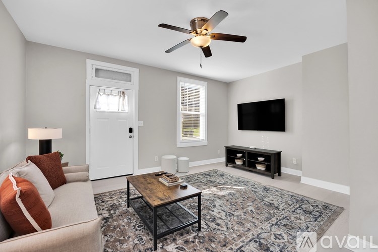 A living room with a couch, a coffee table, a ceiling fan, and a flat screen TV.