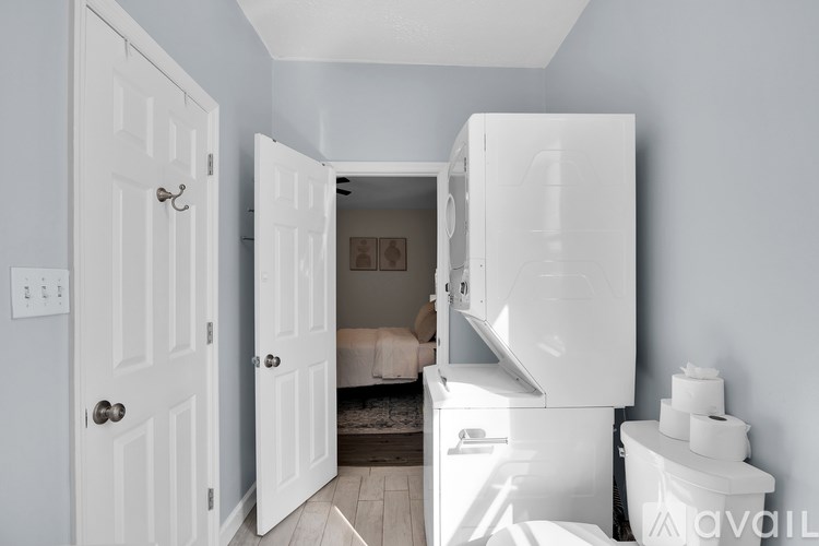 A white door is open to a small room with a bed and a refrigerator.