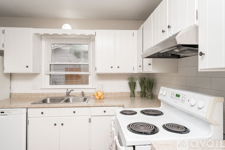 A white stove with four burners is in a kitchen with white cabinets.