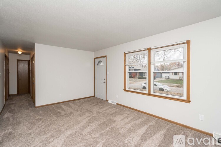 A room with a carpeted floor and a window showing a residential area outside.