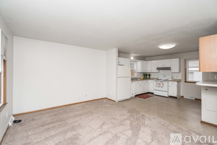 A spacious kitchen and living room with white appliances and a carpeted floor.