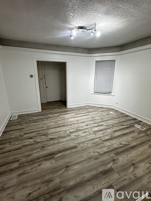 A room with wooden flooring and a door leading to another room.