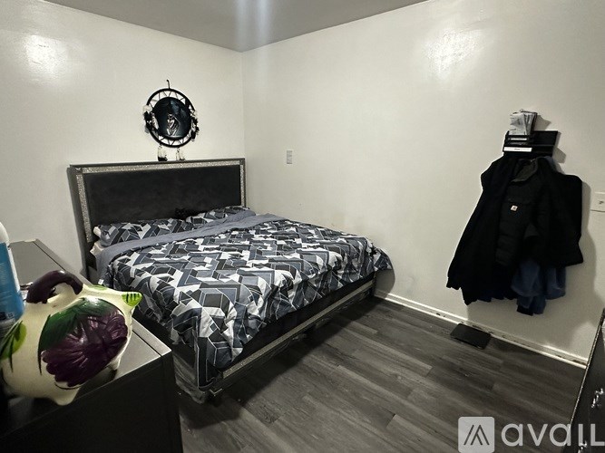A bedroom with a black and white bedspread and a black coat hanging on the wall.