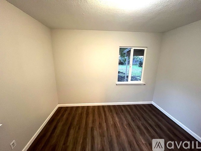 A room with wooden flooring and a window showing a view of a lawn.