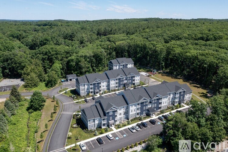 A large building complex with a parking lot in front, surrounded by trees.