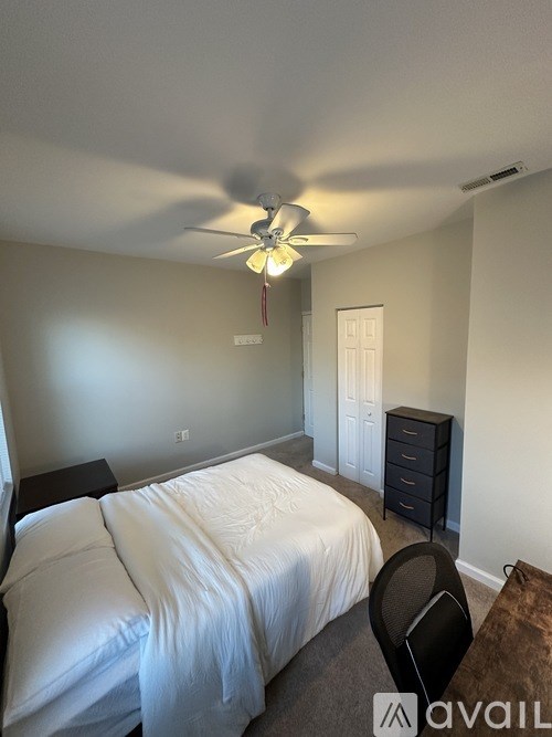 A bedroom with a bed, chair, and ceiling fan.