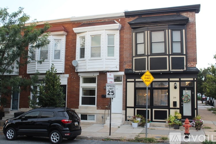 A black car is parked in front of a brick building with a speed limit sign.