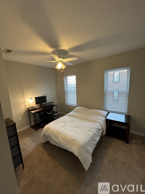 A bedroom with a bed, desk, and a ceiling fan.