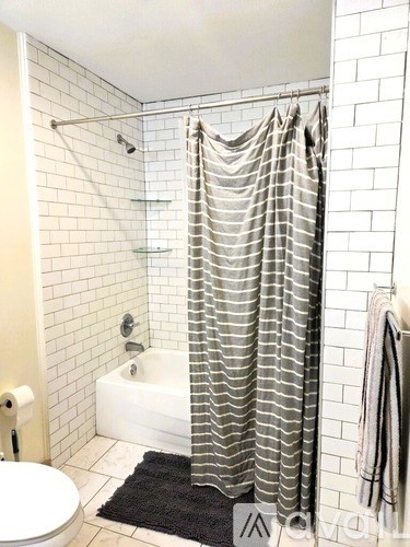 A white tiled bathroom with a black mat and a white bathtub.