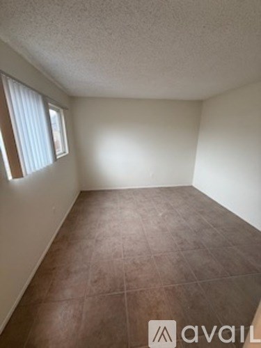 A room with brown tile flooring and a window with blinds.