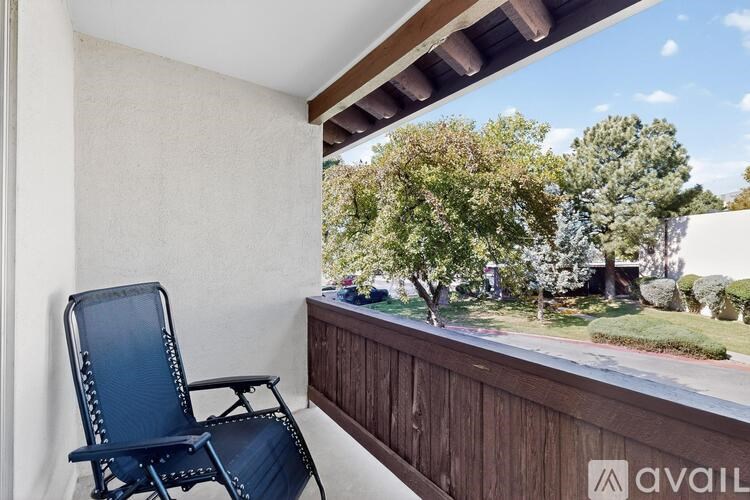 A blue chair is on a balcony with a view of trees and a house.