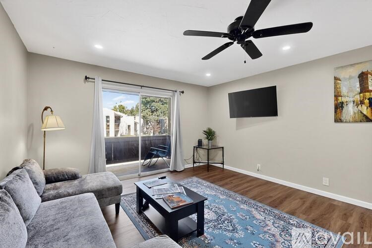 A living room with a grey sofa, a black coffee table, a ceiling fan, and a flat screen TV mounted on the wall.