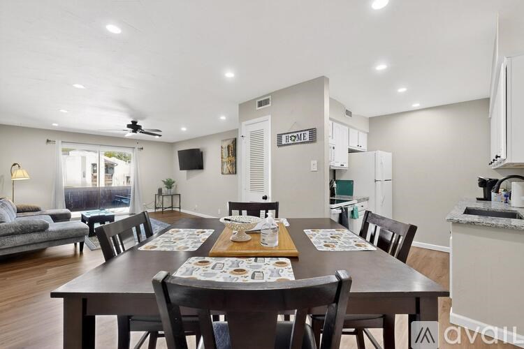 A dining room with a table set for six with a view of the kitchen in the background.