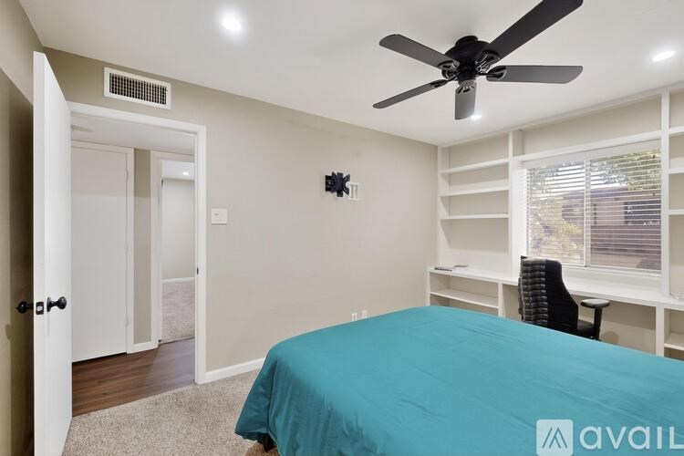 A bedroom with a blue bedspread and a ceiling fan.