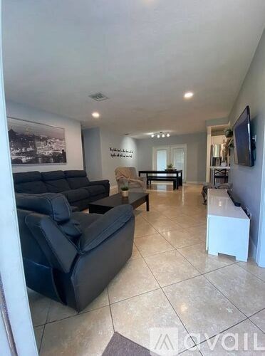 A living room with a black leather sofa and a television on the wall.