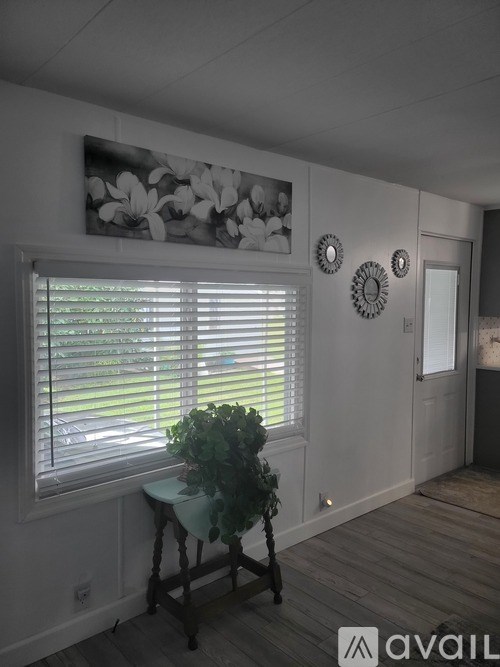 A room with a table and a plant in front of a window with blinds.