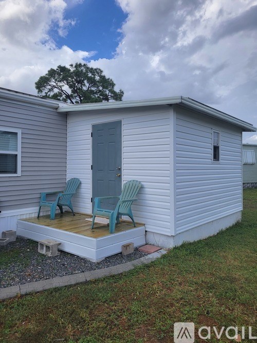 A small house with a grey door and two chairs on the porch.