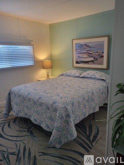 A bed with a blue patterned cover sits in a room with a green wall and a framed picture above it.