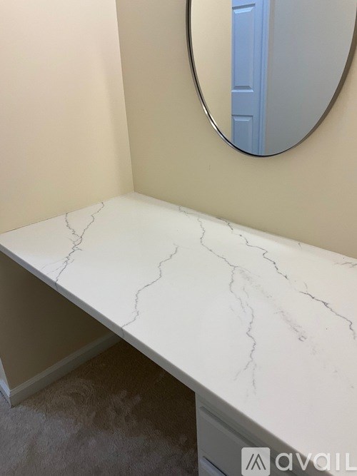 A white marble countertop with a round mirror above it.