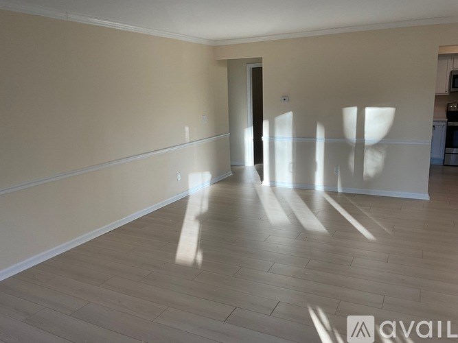 A spacious room with light wood flooring and a door in the background.