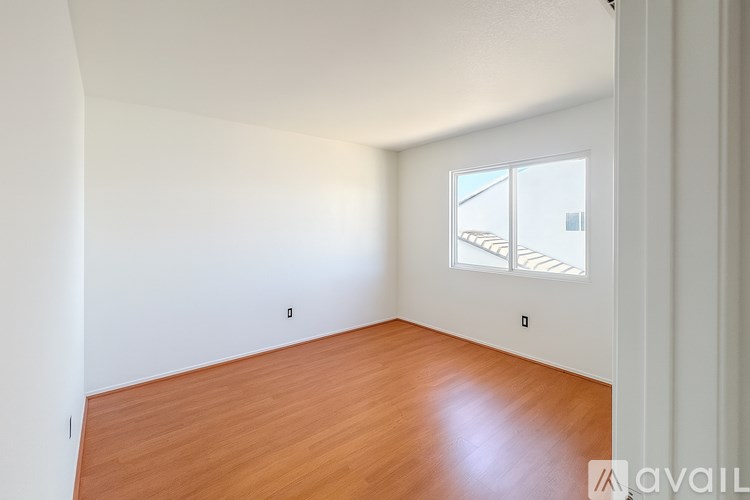 A room with wooden flooring and a window showing a balcony outside.