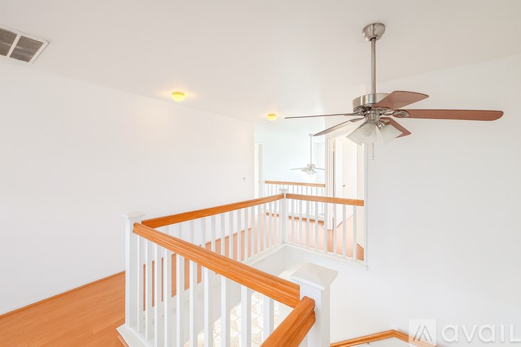 A fan hangs from the ceiling in a white room with a wooden staircase.