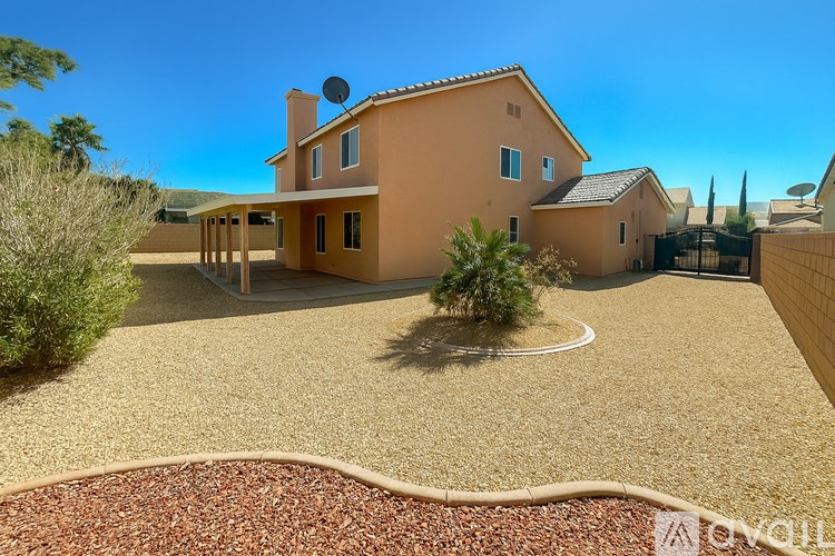 A house with a brown roof and a satellite dish on the roof is surrounded by a gravel driveway and a small garden.