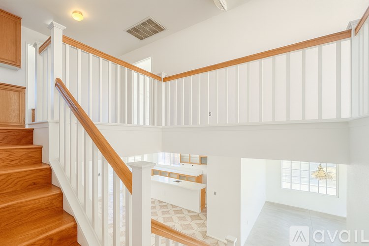A staircase with white railings and wooden steps leads to a bright room with a window.