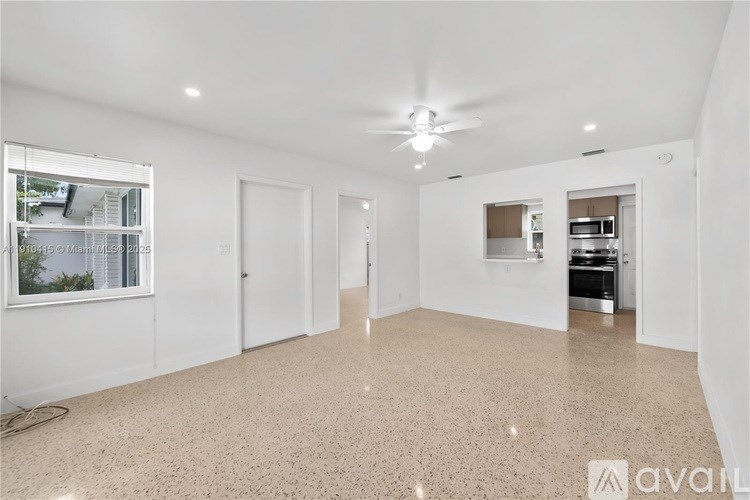 A spacious, empty room with a ceiling fan and a window overlooking a balcony.