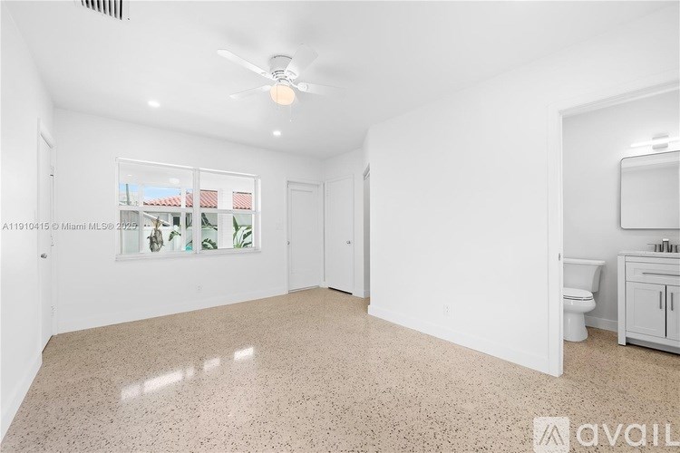 A spacious, empty room with a ceiling fan and a window with a view of a residential area.