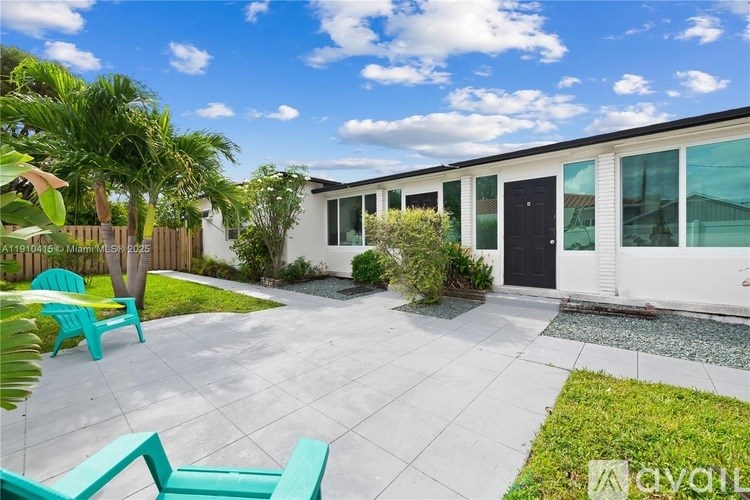 A sunny day at a white house with a patio and green chairs.