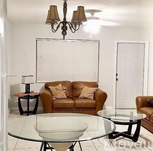 A living room with a brown couch, glass table, and a chandelier.