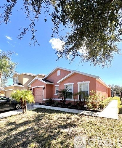 A house with a red roof and white trim is surrounded by a well-maintained lawn and trees.