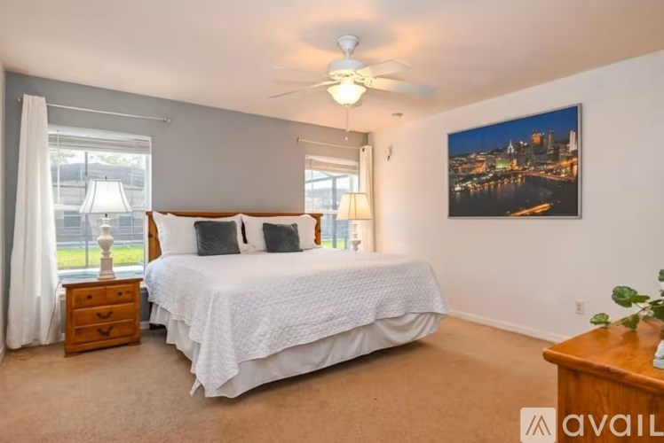 A bedroom with a large bed, a ceiling fan, and a cityscape picture on the wall.