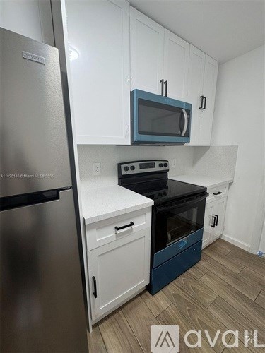 A kitchen with a stainless steel refrigerator, a blue microwave, and a black stove top oven.