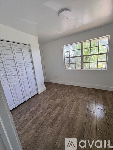 A room with wooden flooring and a window with a view of trees.