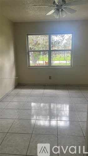 A room with a ceiling fan and a window overlooking a lawn.