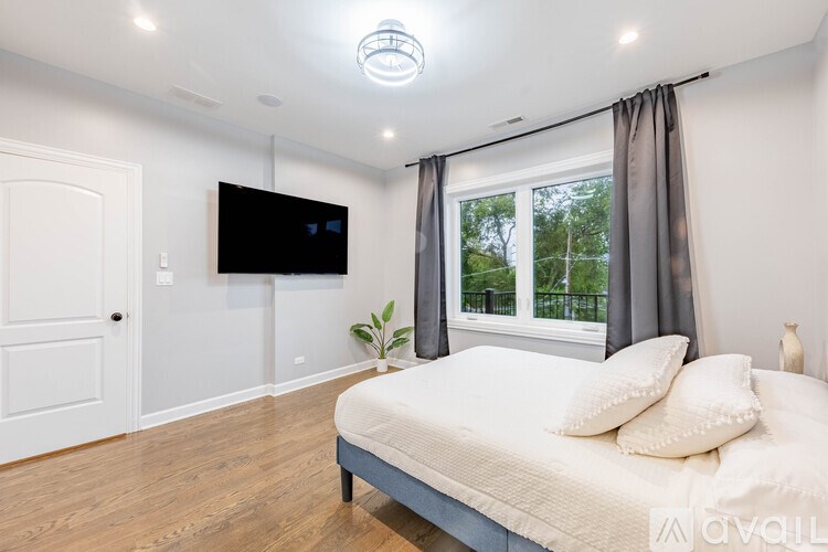 A bedroom with a bed, a television, and a window with curtains.