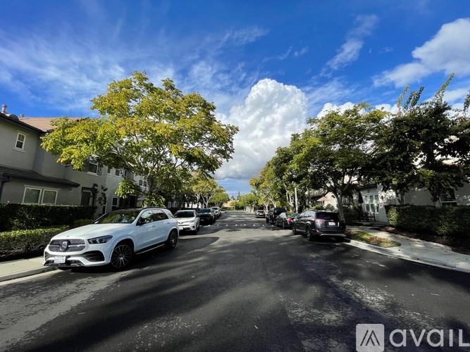 A white car is parked on the left side of a street lined with parked cars and trees.