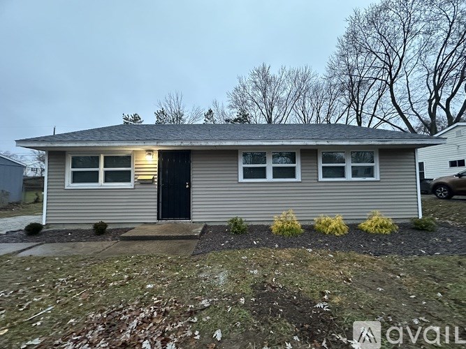 A small house with a black door and windows is surrounded by a gravel area and some small plants.