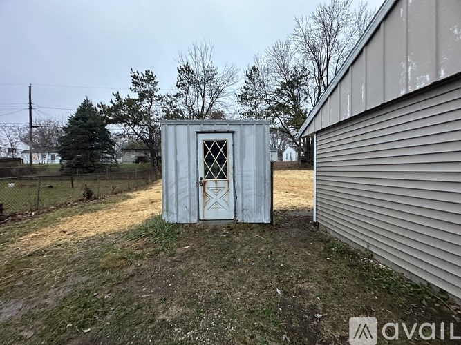 A white shed with a cross design on the door is situated in a grassy area.
