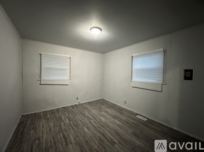 A room with wooden flooring and two windows with blinds.