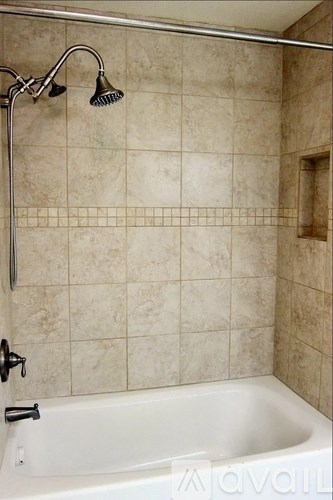 A white bathtub with a shower head and a wall of tiles.