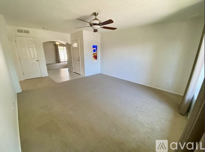 A spacious room with a ceiling fan and light, carpeted floor, and a door leading to another room.