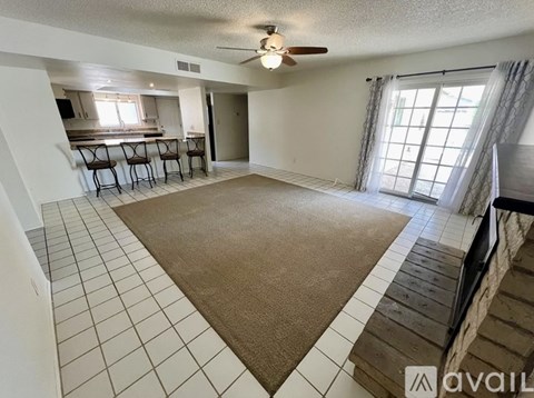 A living room with a brown rug and a ceiling fan.