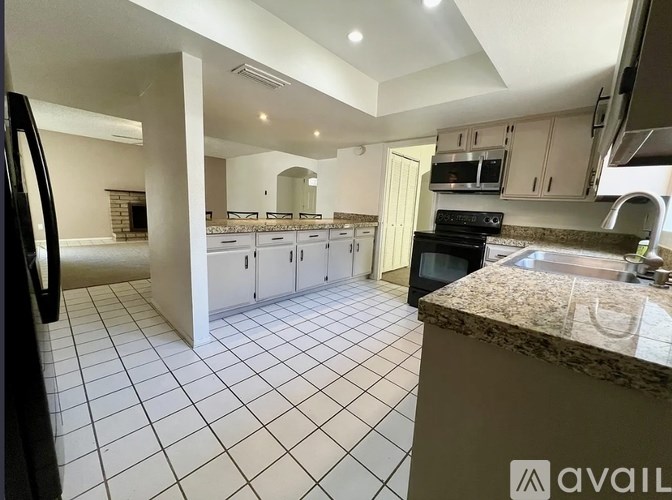 A kitchen with a black fridge, white cabinets, and a granite countertop.
