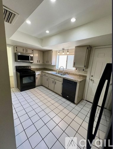 A kitchen with white tiled floors and a black refrigerator.