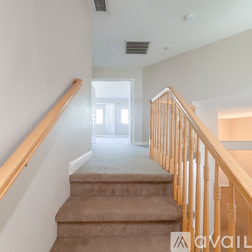 A staircase with a beige carpeted runner and wooden balusters leads to a bright room.