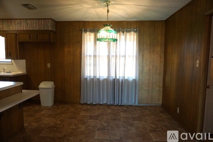 A kitchen area with a trash bin and a window with curtains.